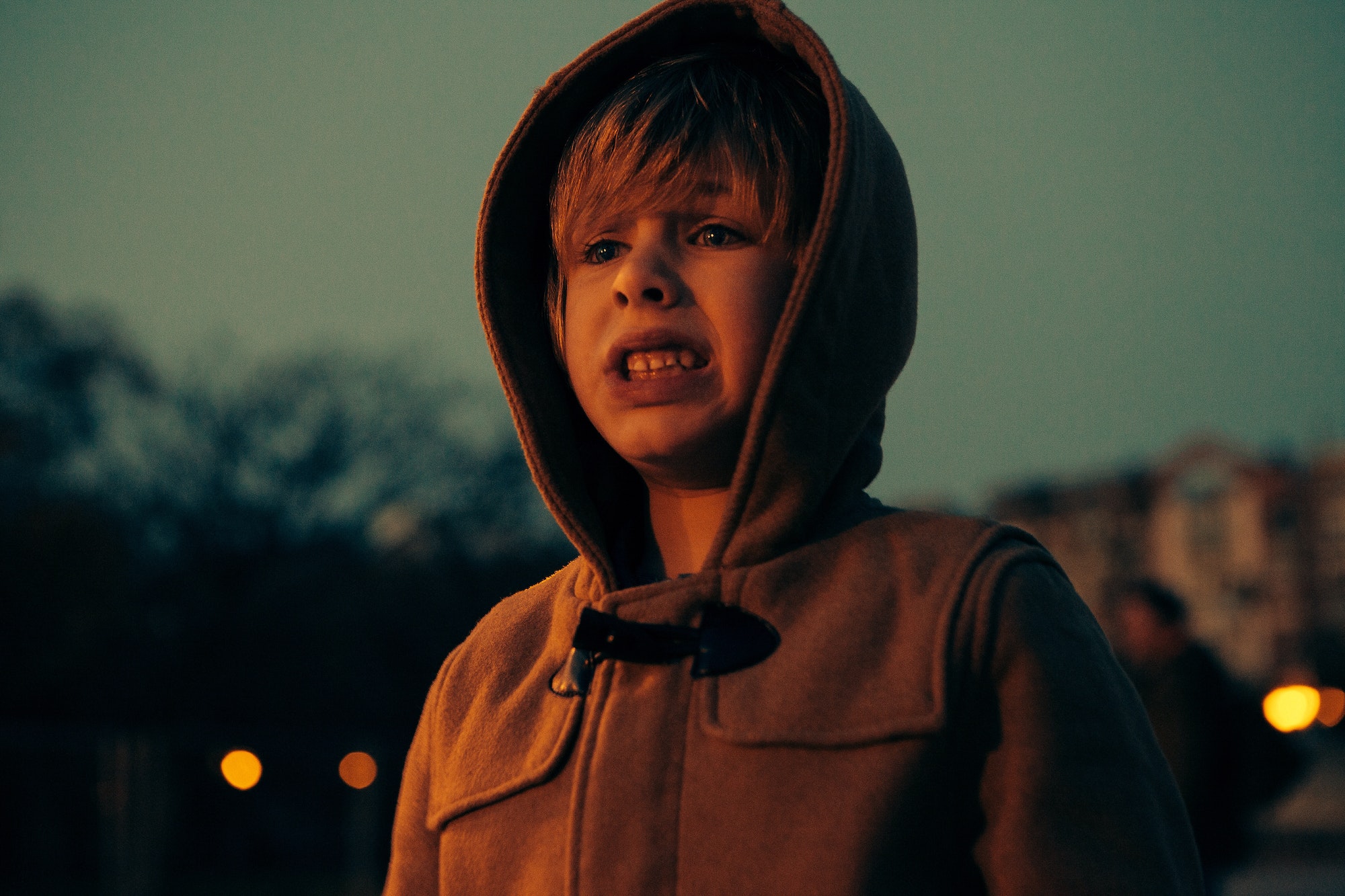 Portrait of a distressed child with a hood over his head at dusk.