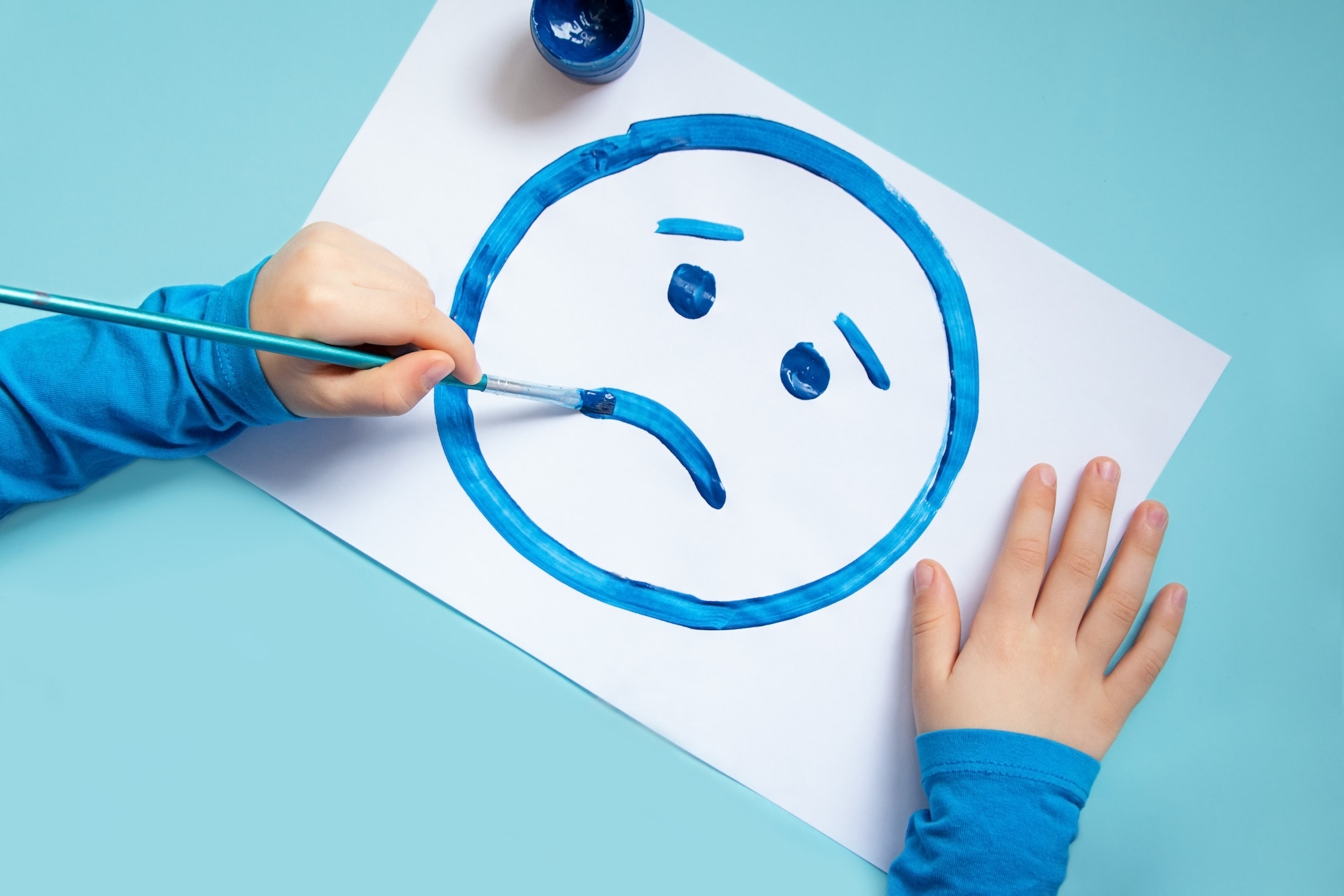 Top view of child drawing sad face. Blue background.